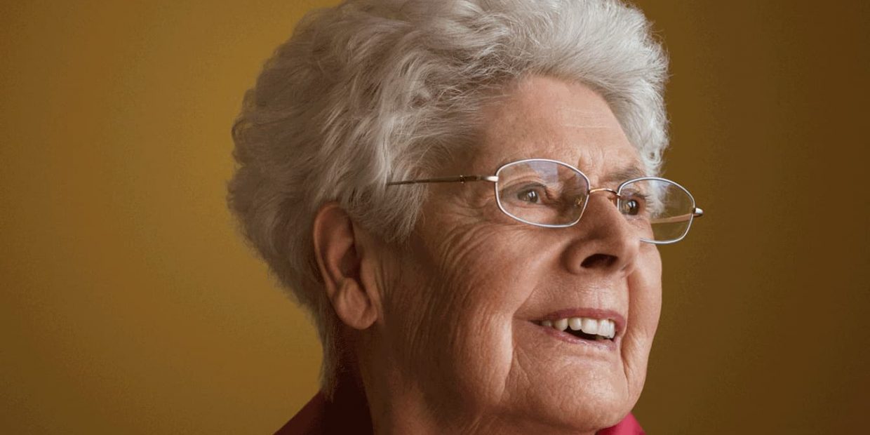 Portrait einer alten Dame mit weissen Harren und Brille, die lächelt.