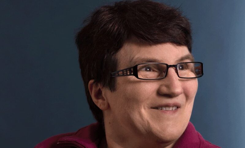 Ritratto di una signora con capelli castani e occhiali sorridenti.